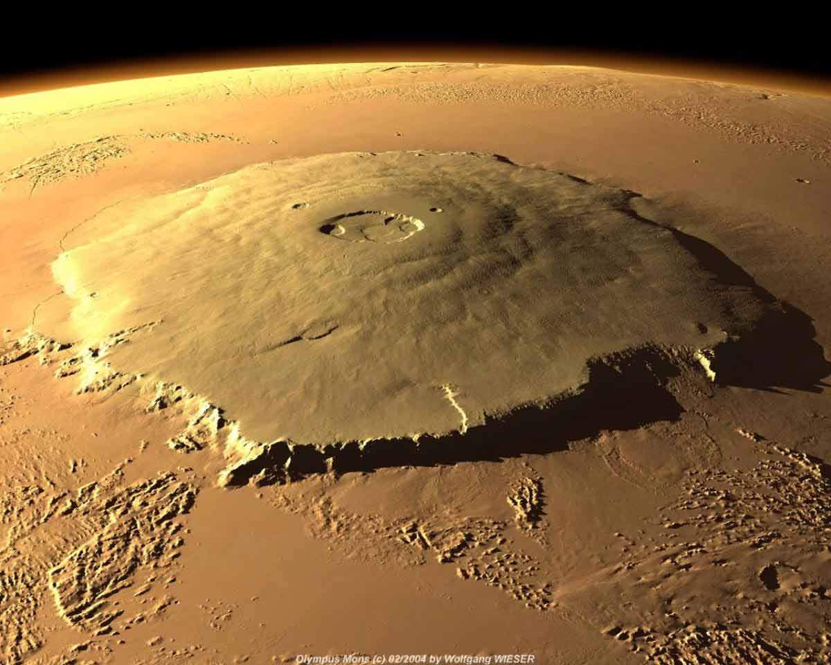 A satellite image of Olympus Mons, Mars, the largest volcano in the solar system at about three times the height of Mount Everest. Around 3.5 to 4.0 billion years ago, the release of volcanic gases, especially the greenhouse gas sulfur-dioxide, may have warmed the surface of Mars episodically, thereby explaining the presence of geomorphological features indicative of the flow of water on the planet's ancient surface